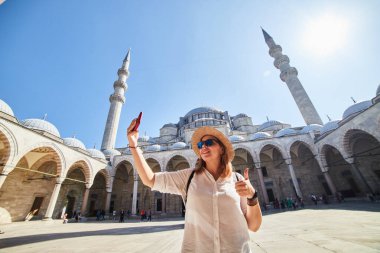 İstanbul, Türkiye - 14 Ekim 2019: Şapkalı mutlu çekici kadın turist, Süleyman camisinin avlusunda poz veriyor ve fotoğraf çekiyor. Din ve seyahat kavramı.