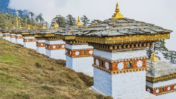 Dochula pass 108 chortens (estupas asiáticas) es el monumento en honor de los soldados butaneses en la ciudad de Timpu con el paisaje de hierba y el fondo nublado del cielo, Bután — Foto de Stock