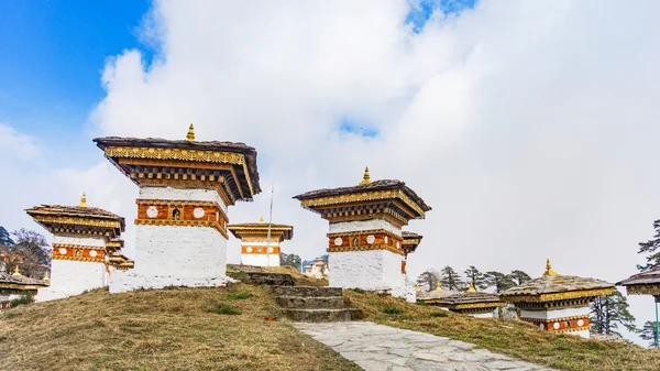 Dochula pass 108 chortens (estupas asiáticas) es el monumento en honor de los soldados butaneses en la ciudad de Timpu con el paisaje de hierba y el fondo nublado del cielo, Bután — Foto de Stock