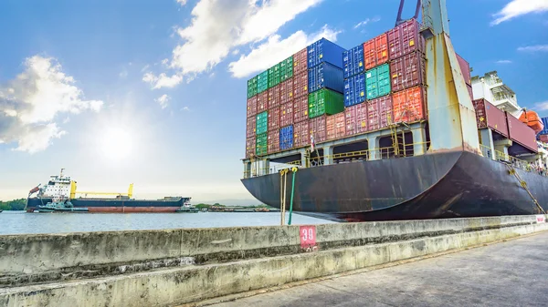 De containers lading op het schip van de container in de haven met de rivier en de zee en de bewolkte hemel. — Stockfoto