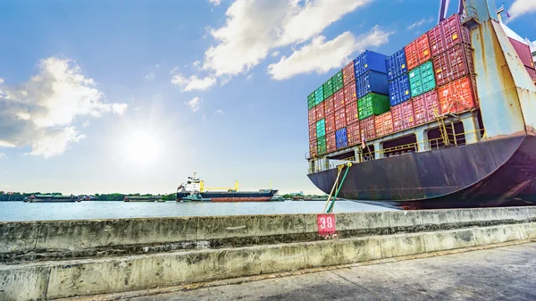 De containers lading op het schip van de container in de haven met de rivier en de zee en de bewolkte hemel. — Stockfoto
