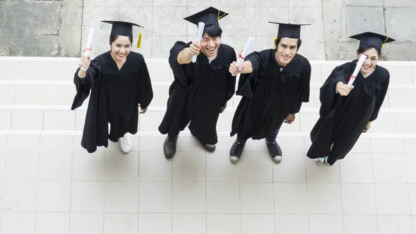 Ovanifrån av människor studenter examen klänningar och hatt stå och innehar examensbevis känslan av glad och graciös. — Stockfoto