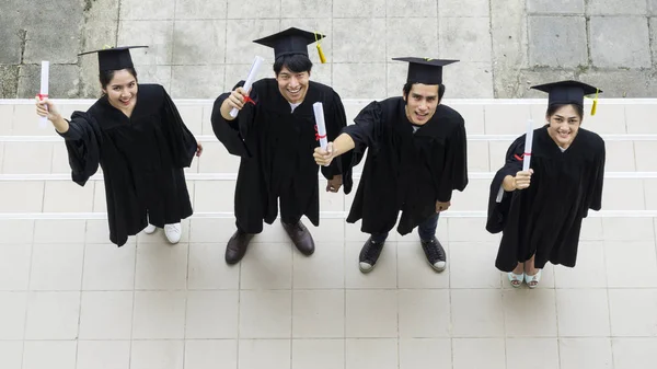 Ovanifrån av människor studenter examen klänningar och hatt stå och innehar examensbevis känslan av glad och graciös. — Stockfoto