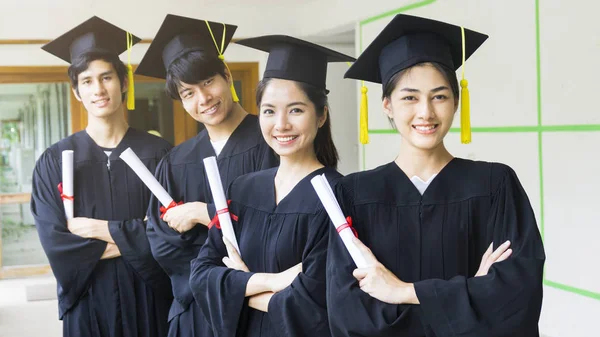 Студенты мужчины и женщины в черных выпускных платьях держат диплом и стоят вместе. С чувством счастья и изящества . — стоковое фото