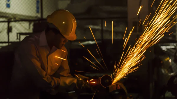 O trabalhador usa máquina de corte para cortar metal, foco na linha de luz de flash de faísca afiada, em baixa luz — Fotografia de Stock