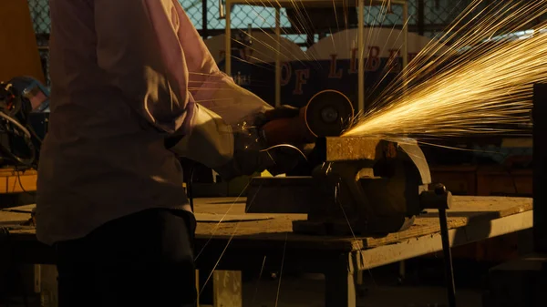 O trabalhador usa máquina de corte para cortar metal, foco na linha de luz de flash de faísca afiada, em baixa luz — Fotografia de Stock