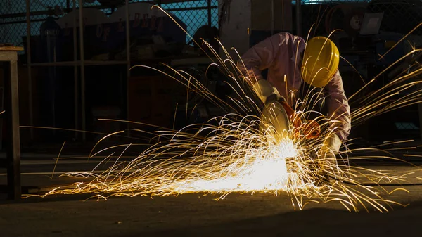Dělník používá řezací stroj k řezání kovu, soustředí se na světelnou linii ostré jiskry, za slabého světla — Stock fotografie
