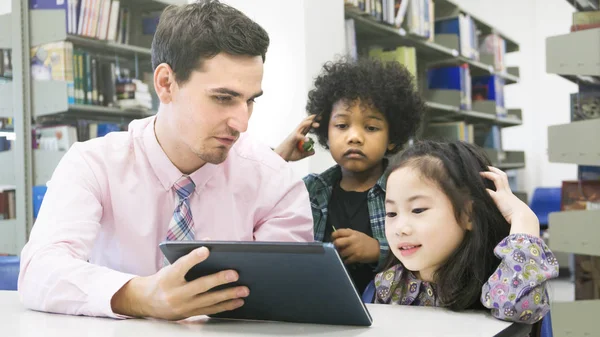 Hombre profesor y niños estudiantes de aprendizaje y mirando en el dispositivo de tableta con el libro de sí mismo en el fondo — Foto de Stock