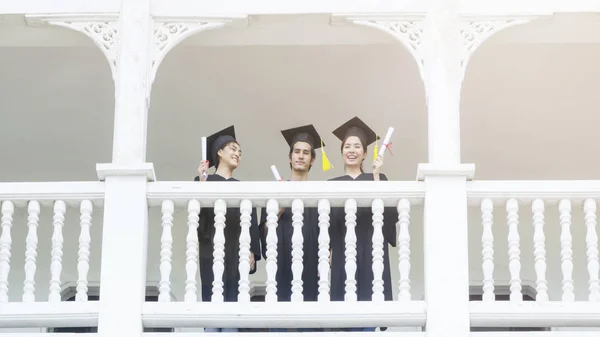 Människor studenter i känslan av glad och graciös med examen klänningar och cap står i raden på korridoren av klassisk byggnad. — Stockfoto