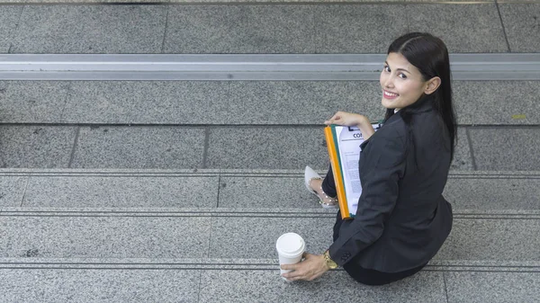 Retrato de mulher de negócios inteligente senta-se e trabalha com a xícara de bebida no caminho pedestre ao ar livre na parte da manhã — Fotografia de Stock