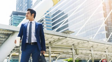 İş portresi Asyalı adam elinde bir bardak içkiyle yaya geçidinde duruyor.