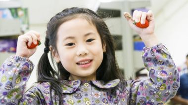 Gülen komik Asya sevimli kız ayakta ve tutun meyve çilek