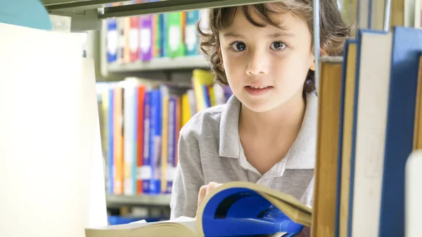 Sonriente chico blanco con el libro y la estantería en el fondo — Foto de Stock