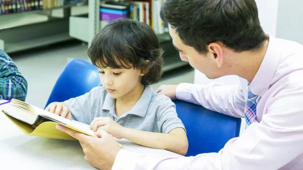 Учитель и мальчик учатся с книгой на книжной полке — стоковое фото