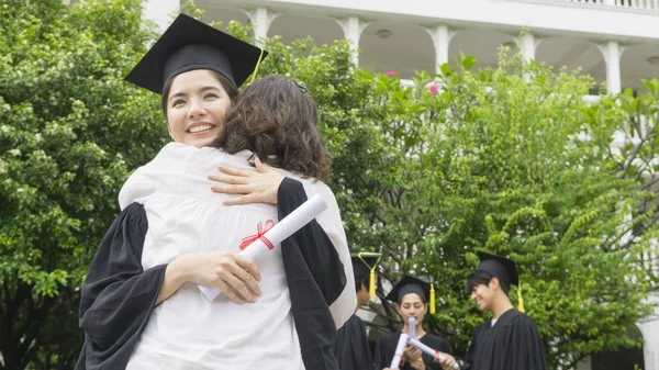 Studente ragazza con gli abiti di laurea e cappello abbracciare il genitore nella cerimonia di congratulazione . — Foto Stock