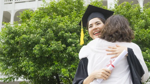 Studente ragazza con gli abiti di laurea e cappello abbracciare il genitore nella cerimonia di congratulazione . — Foto Stock