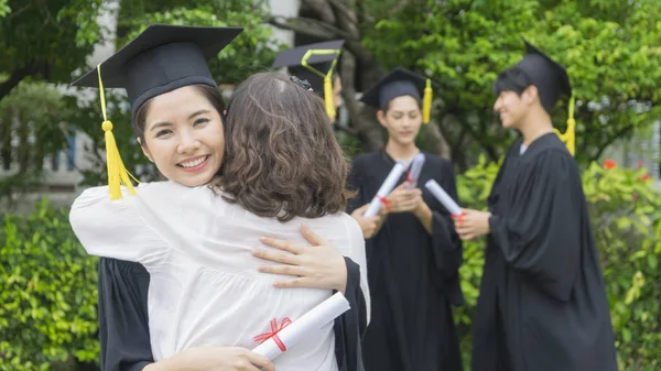 Κορίτσι φοιτητής με την αποφοίτηση φορέματα και καπέλο η μητρική αγκαλιά στην τελετή συγχαρητήρια. — Φωτογραφία Αρχείου