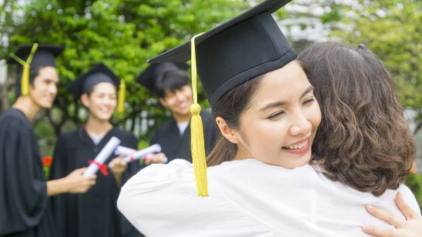 여자 학생 졸업 가운과 모자와 포옹 부모 축 하 행사에. — 스톡 사진