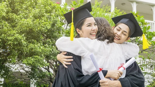 Due donne asiatiche sorridono e si sentono felici in abiti di laurea e berretto e stare con il genitore nel braccio abbraccio — Foto Stock