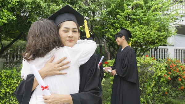 Studente ragazza con gli abiti di laurea e cappello abbracciare il genitore nella cerimonia di congratulazione . — Foto Stock