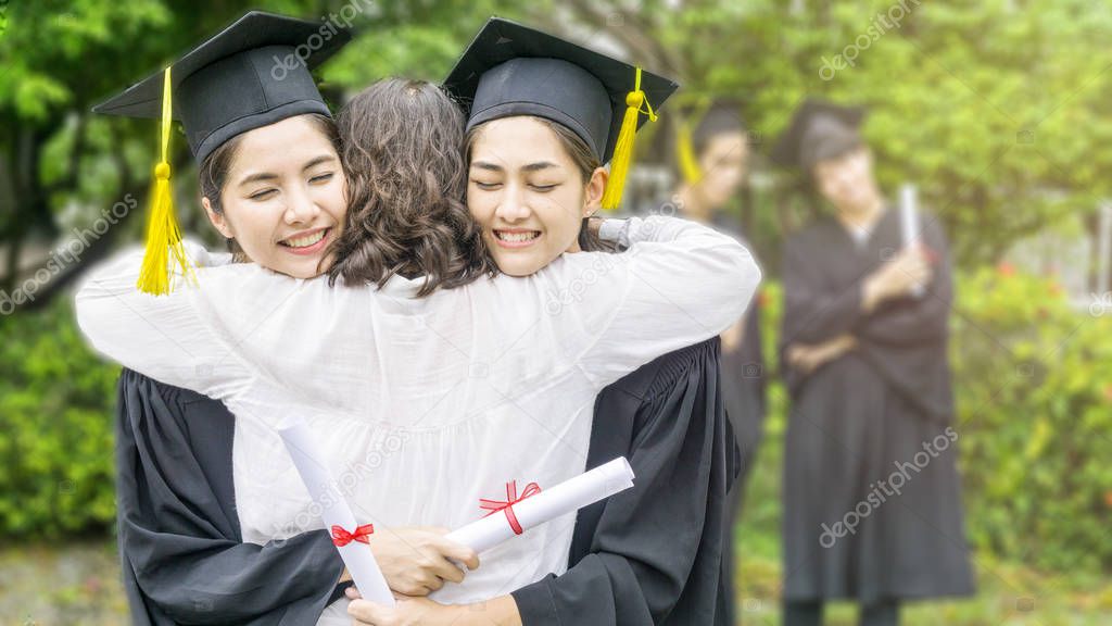 two asian women smiles and feel happy in  graduation gowns and cap and stand with the parent in the arm hug