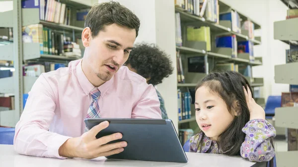 Hombre profesor y niño estudiante aprendizaje y mirando en el dispositivo de la tableta con el libro del uno mismo en el fondo — Foto de Stock