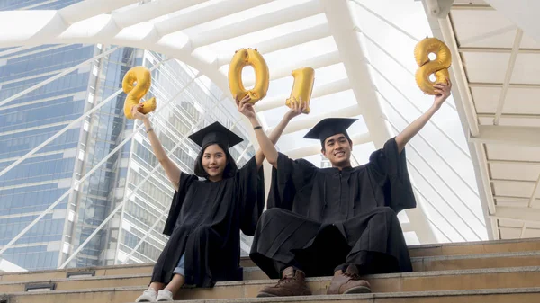 Studenti in abito di laurea sedersi e palloncini numero d'oro 2018 — Foto Stock