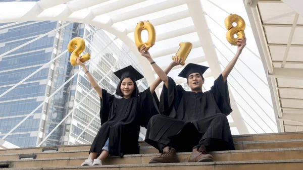 Studenti in abito di laurea sedersi e palloncini numero d'oro 2018 — Foto Stock
