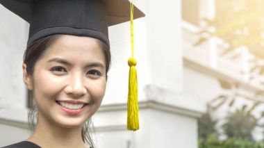 Bayan öğrenci gülümser ve mezuniyet elbisesi ve şapkasıyla mutlu olur.