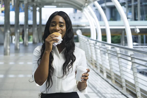 Portrait of happy business black woman eats on hold fast food