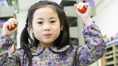 Gülen komik Asya sevimli kız ayakta ve tutun meyve çilek