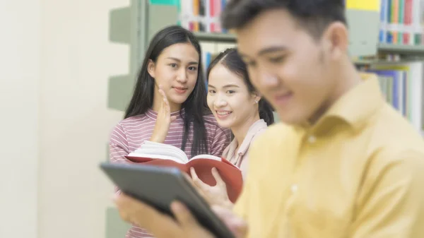 Asiático adolescente homem lê um tablet com meninas falar no o livro sh — Fotografia de Stock