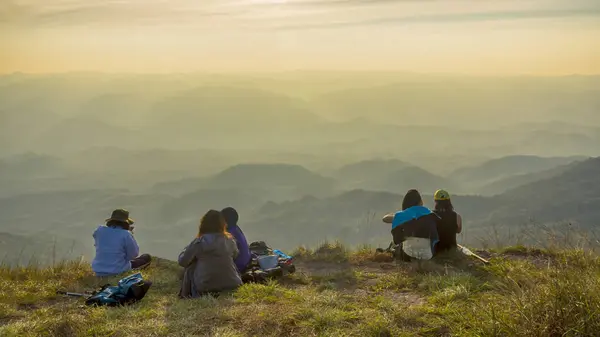 As pessoas caminhantes descansam e sentam-se no pico da montanha.com o vale do nevoeiro da montanha do outono. sol da manhã brilhante brilhando no céu . — Fotografia de Stock