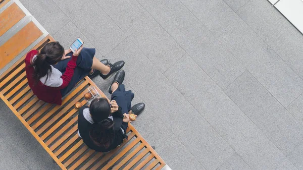 Vista superior de las niñas grupo de usar el teléfono inteligente y hablar en el banco de madera —  Fotos de Stock