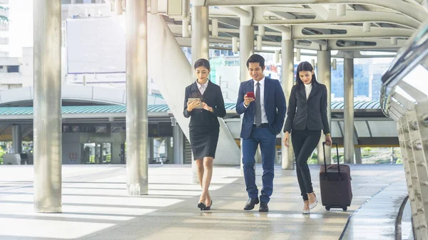 Squadra di uomini e donne intelligenti uomini e donne d'affari camminano nelle ore di punta a piedi pedonale all'aperto e parlano insieme con tablet dispositivo smartphone e bagagli con l'edificio dello spazio urbano — Foto Stock