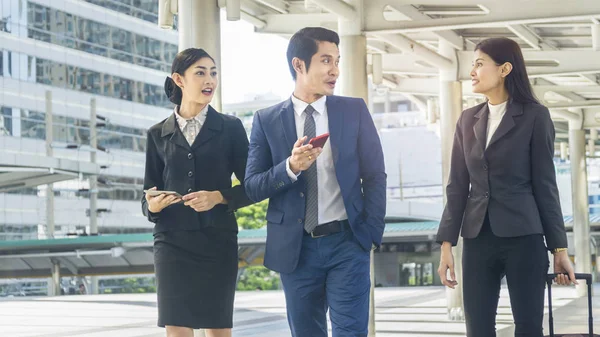 Equipo de gente de negocios hombre y mujer inteligentes caminan en hora punta en camino peatonal al aire libre y hablan junto con el dispositivo de teléfono inteligente tableta y el equipaje con el edificio del espacio de la ciudad — Foto de Stock