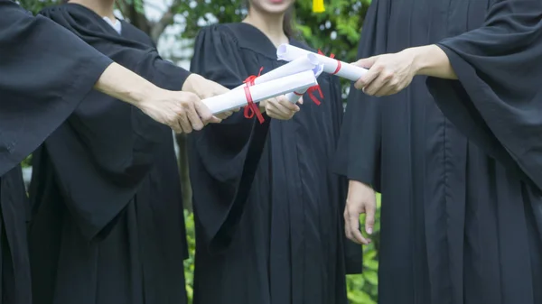 Personer med svarta examen klänningar innehar diplom. — Stockfoto