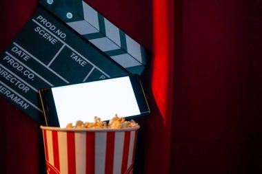 Boş beyaz ekranlı cep telefonu, patlamış mısır kovası ve film alkışlama tahtası. İnternet telefonunda TV yayını kavramı.