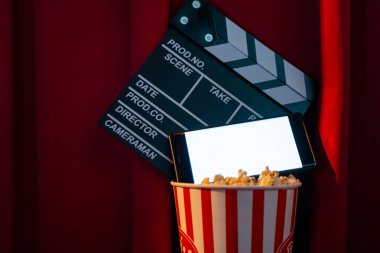 Boş beyaz ekranlı cep telefonu, patlamış mısır kovası ve film alkışlama tahtası. İnternet telefonunda TV yayını kavramı.