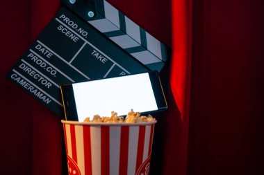 Boş beyaz ekranlı cep telefonu, patlamış mısır kovası ve film alkışlama tahtası. İnternet telefonunda TV yayını kavramı.