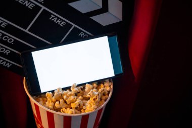 Boş beyaz ekranlı cep telefonu, patlamış mısır kovası ve film alkışlama tahtası. İnternet telefonunda TV yayını kavramı.