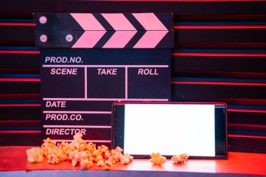 Boş beyaz ekranlı cep telefonu, patlamış mısır kovası ve film alkışlama tahtası. İnternet telefonunda TV yayını kavramı.