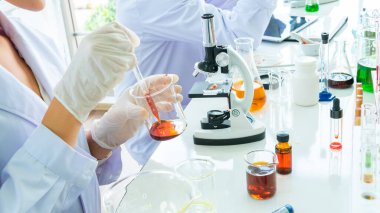 Bilim adamının elini tüple, şişeyle ve mikroskopla kapat. Tüpün ön planı ve sıvı madde kapsülüyle.