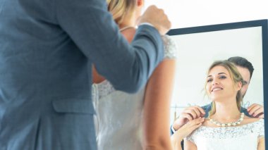 Damat ve kadın gelin mücevher kolye takıyor. Mutlu bir aşkla ve soyunma odasındaki yansıtıcı camlara bakarak..