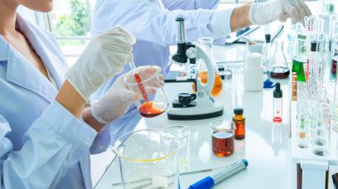 Bilim adamının elini tüple, şişeyle ve mikroskopla kapat. Tüpün ön planı ve sıvı madde kapsülüyle.