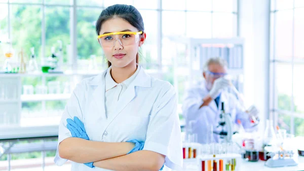 Professor woman researcher white gown stands confident with face concentration. With background interior white lab and the senior scientist prepares testing with equipments on desk.