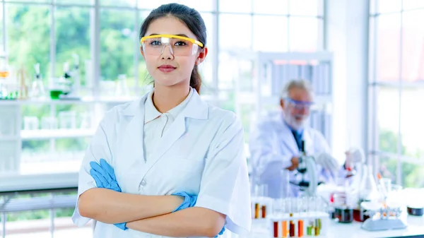 Professor woman researcher white gown stands confident with face concentration. With background interior white lab and the senior scientist prepares testing with equipments on desk.