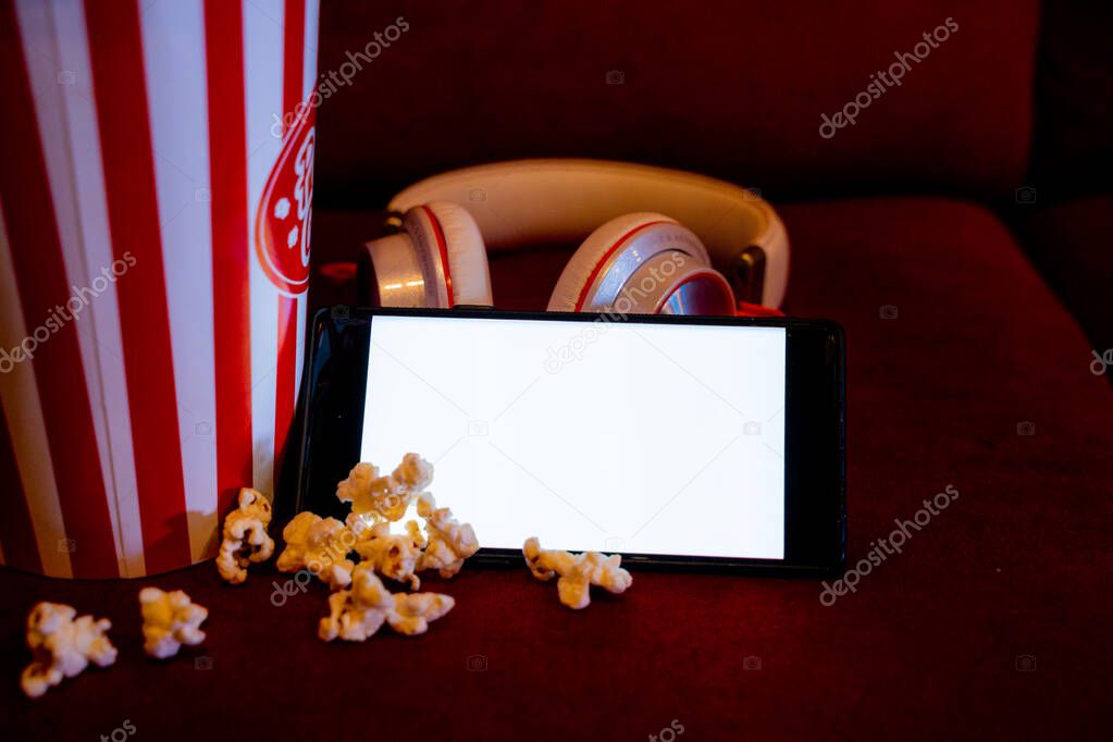 mobile phone with empty white bright screen with popcorn bucket on the red sofa. Concept of streaming TV on internet phone.