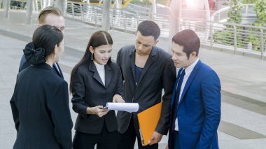 Çok uluslu iş adamları. Zeki erkek ve kadınlar konuşur ve projeyi sunarlar. Evrak işleri ile birlikte şehir meydanındaki modern bina boyunca yaya yürüyüşünde iyi hissedersiniz.