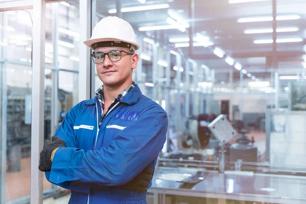 El işçisinin portresi, yüksek teknoloji temiz endüstri fabrikasının cam duvarının önünde mavi çalışma odası elbisesi ve güvenlik kaskıyla ayakta duruyor..